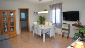 A dining area with a table and chairs, a cabinet with glass doors, a television on the wall, and a plant on the windowsill. - SAONA VILLAS (VN THAI): villa for 12 people, private pool, wifi (Les Tres Cales)