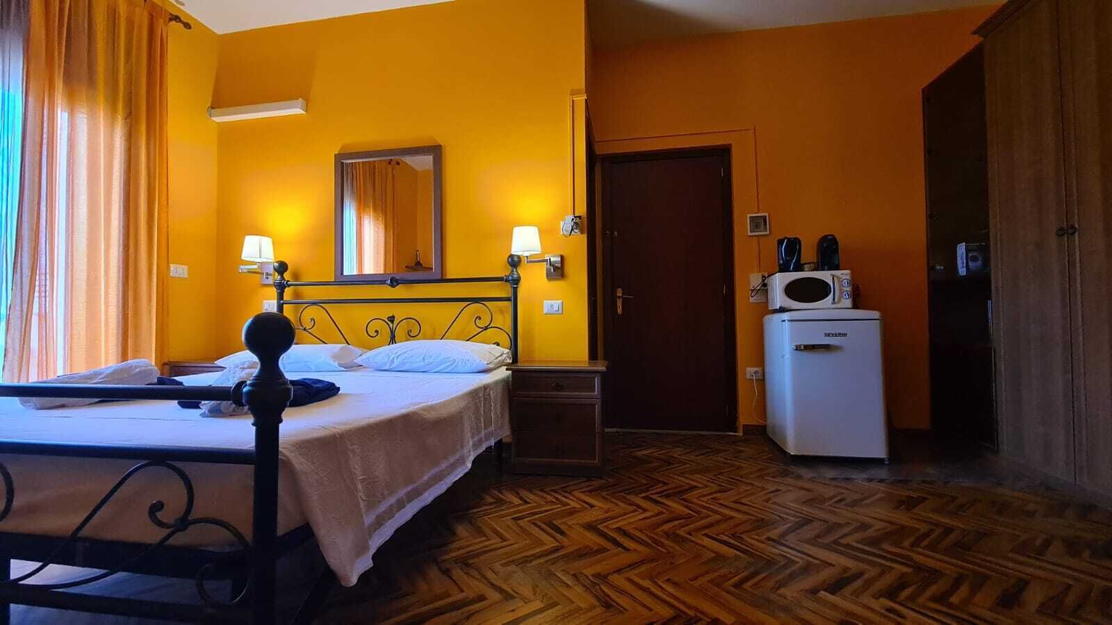 Una habitación de hotel con cama, lámparas de noche, un espejo, una puerta y un refrigerador.