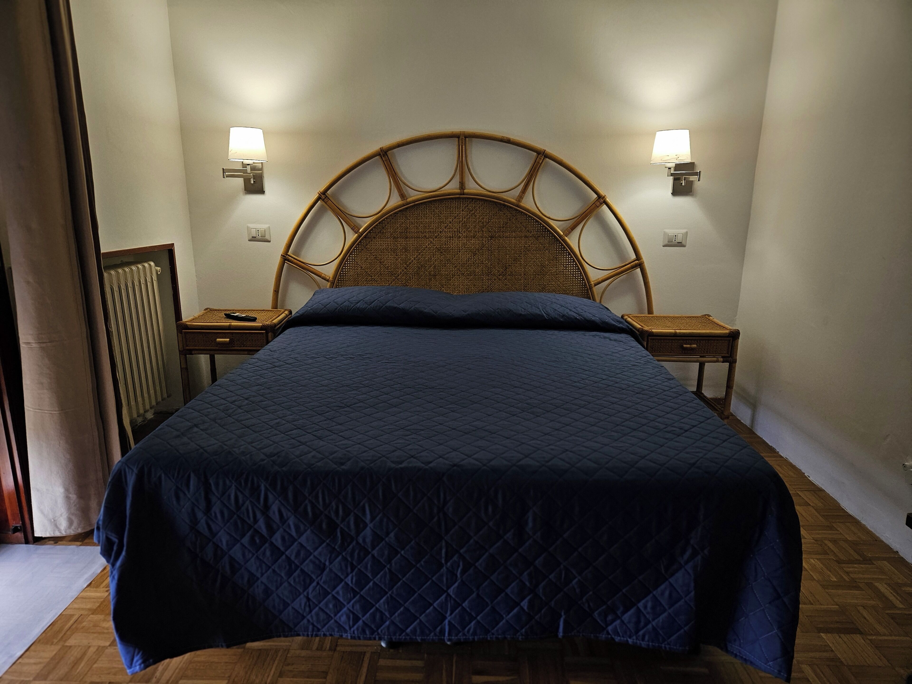 Una cama con cabecera, dos mesitas de noche y lámparas de pared.