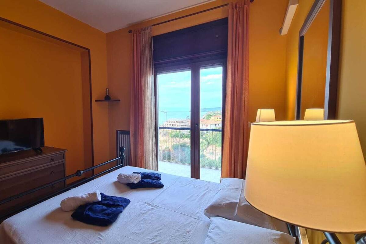 Une chambre d’hôtel avec un lit, un téléviseur posé sur une commode, une fenêtre avec des rideaux et une lampe.