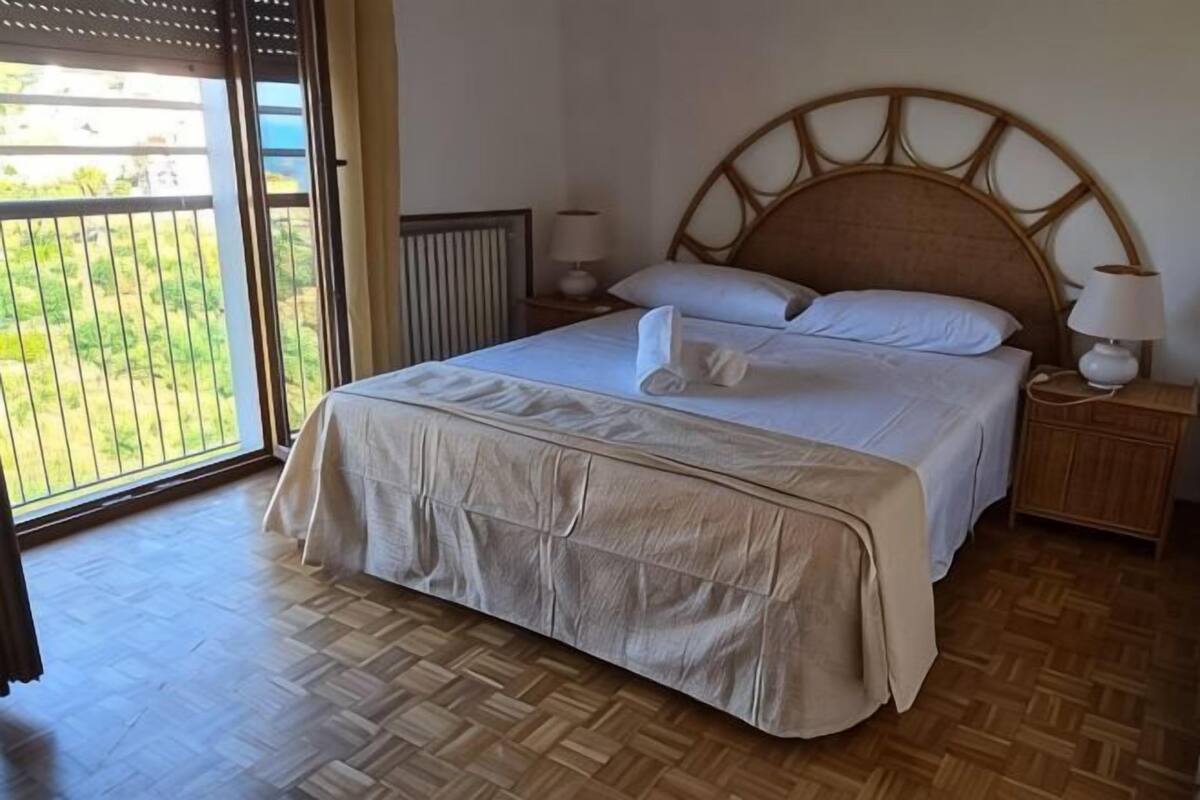 Une chambre à coucher comprenant un lit, une table de chevet, une lampe, une fenêtre donnant sur un beau paysage et un radiateur.