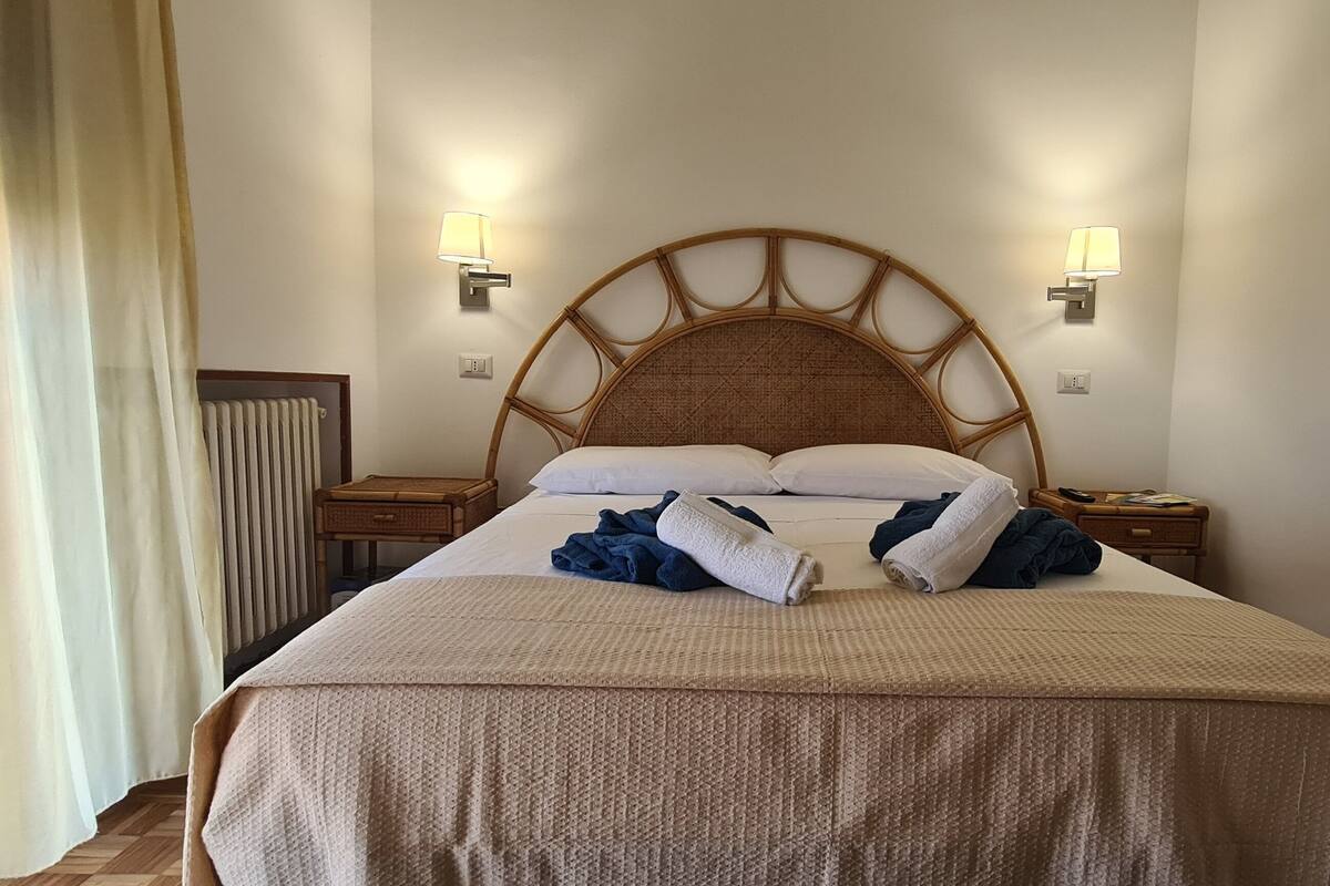 Un lit bien fait, avec une tête de lit, deux lampes de chevet et une table de chevet avec une lampe.