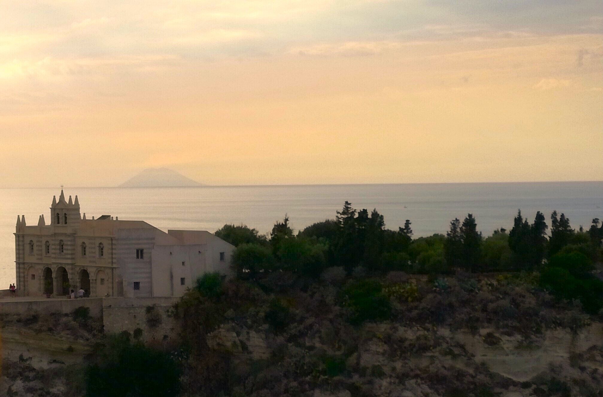 A coastal building with a prominent tower, situated on a rocky terrain with trees in the foreground.