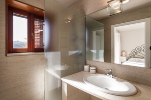 A modern bathroom with a large mirror, a white sink, and a window with blinds. - Near the beach, Maìa panoramic suite for two people (Porto Taverna)