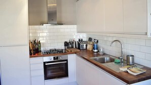 Uma cozinha moderna com armários brancos, coifa de aço inoxidável, forno embutido, bancada de madeira e pia com torneira.