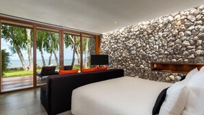 A bedroom with a stone wall, a bed, a TV, and a view of the ocean.