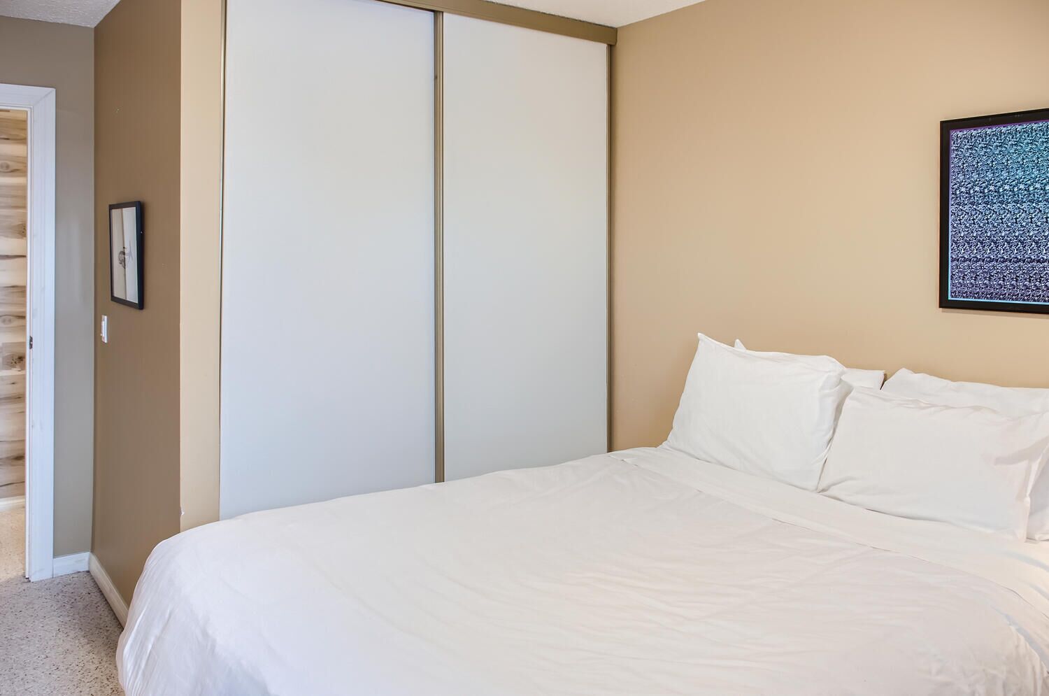 Een slaapkamer met een bed, een kledingkast en een lijst met een afbeelding aan de muur.