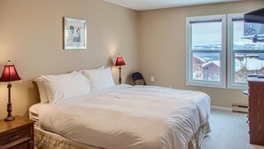 Une chambre avec un grand lit, deux lampes de chevet, une chaise, une fenêtre donnant sur un beau paysage et un tableau encadré au mur.