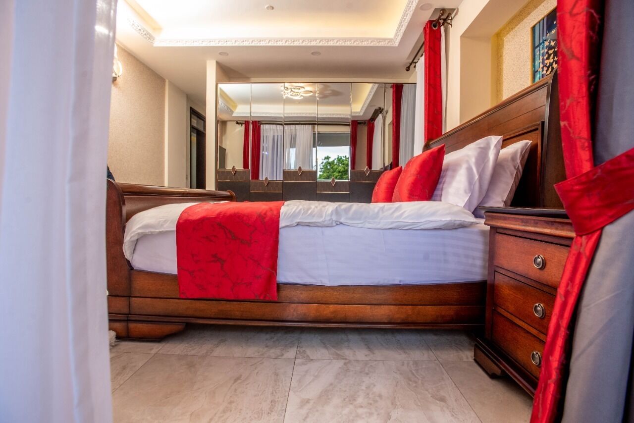 Een slaapkamer met een houten bed, rode gordijnen, een spiegel en een dressoir.