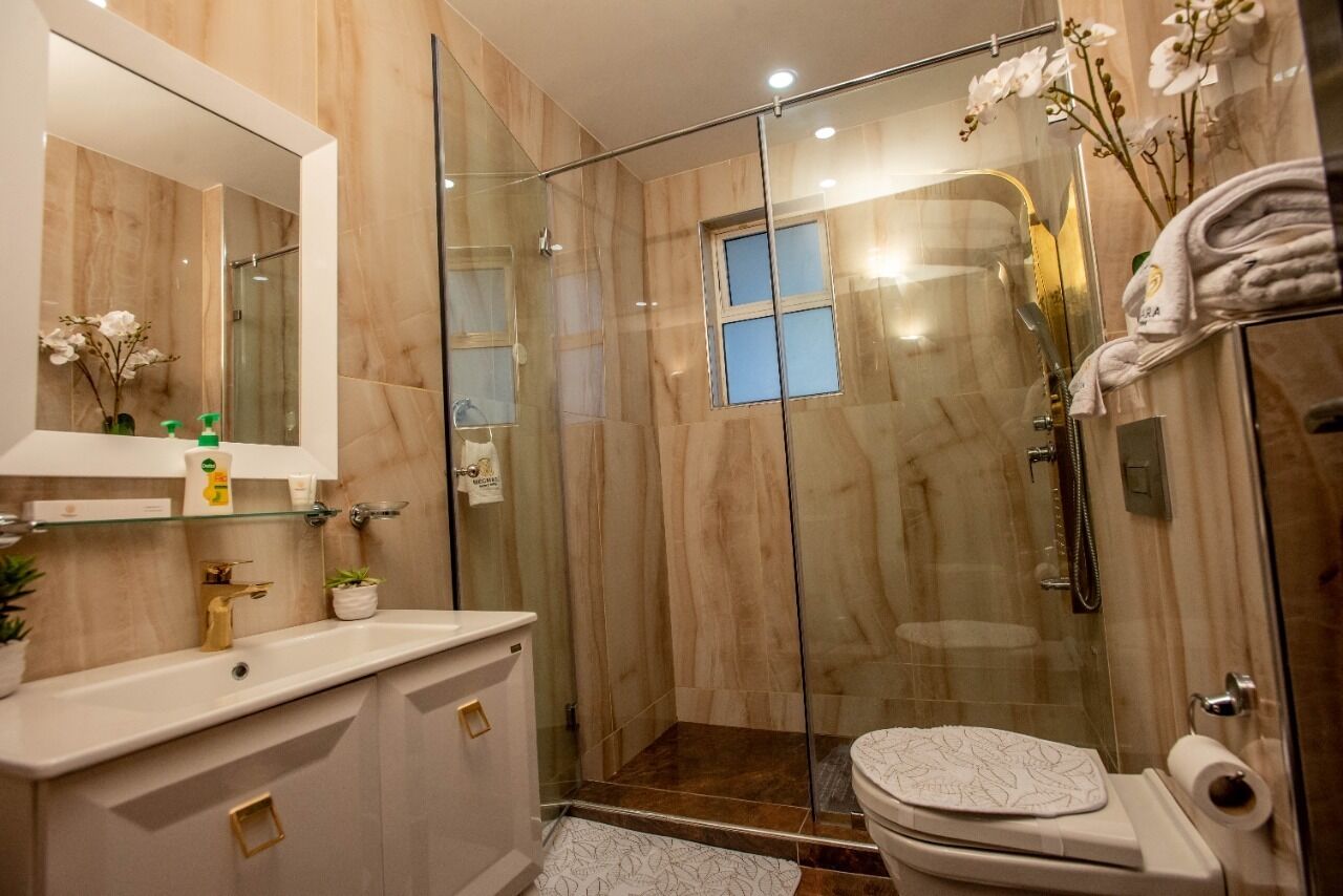 Ein modernes Badezimmer mit einer Glaskabine zur Dusche, einem Waschtisch mit Spiegel und einer Toilette.