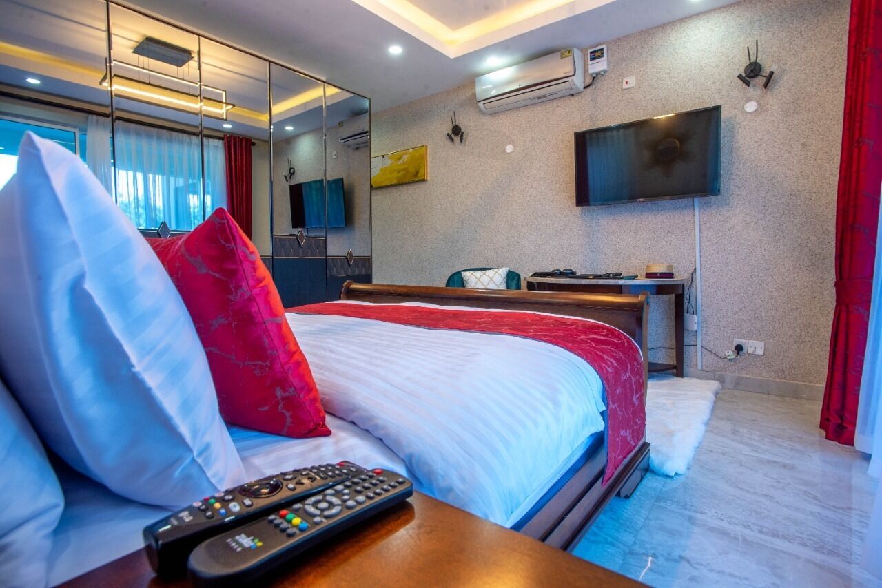Una habitación de hotel con una cama grande, una mesita de noche, un televisor y un espejo.