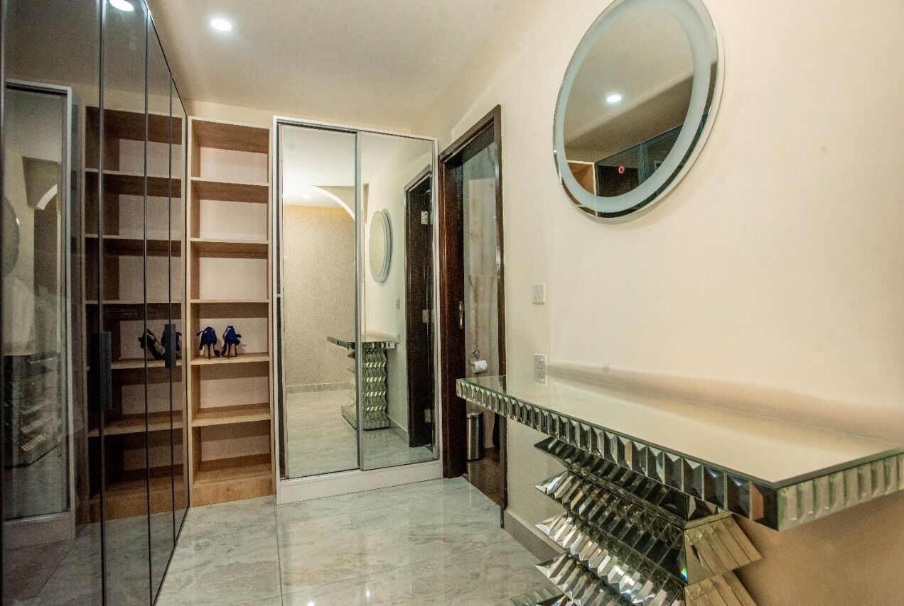 Un interior moderno con un armario de puertas de cristal, un espejo redondo y suelo de mármol.