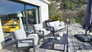 An outdoor seating area with modern furniture, a glass door leading to a room, and a view of a hillside. - Maison Contemporaine Avec Piscine, vue Dégagée (Draguignan)