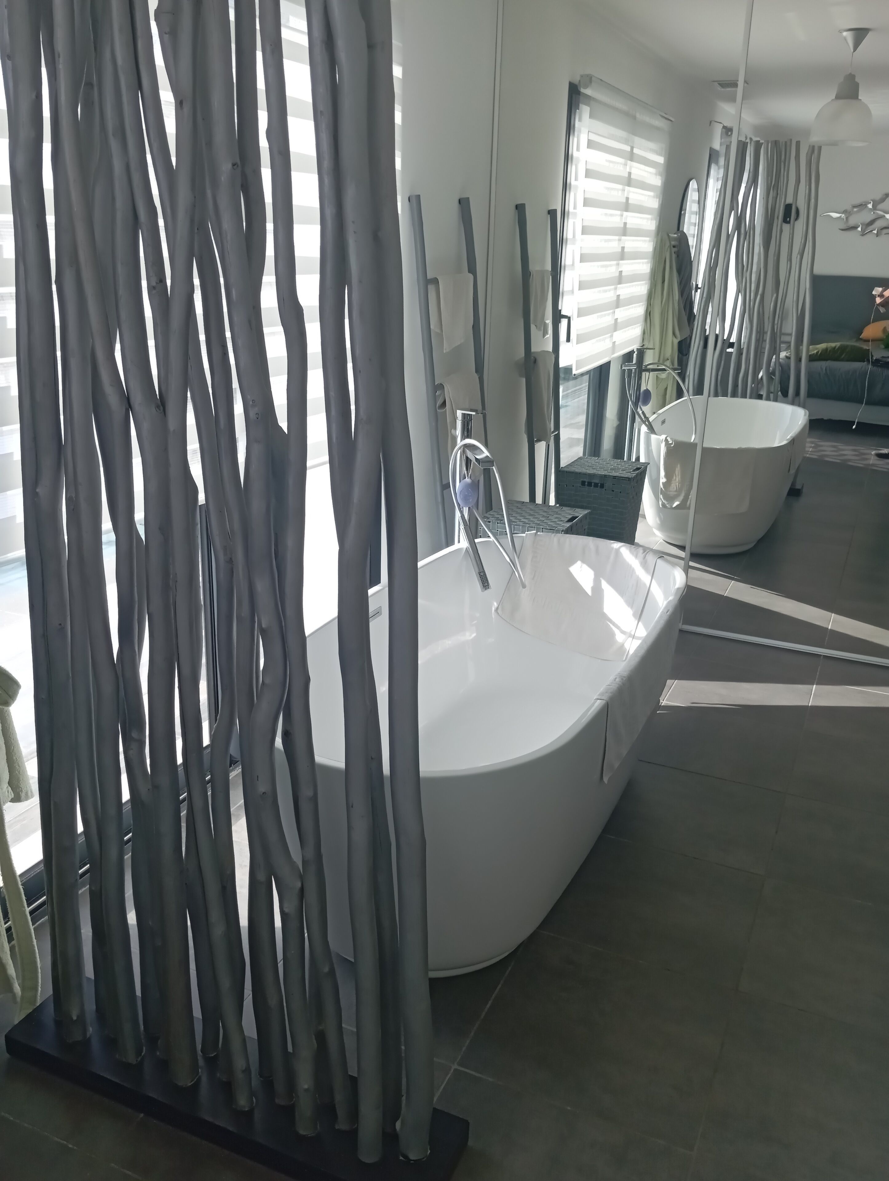 A modern bathroom with a freestanding bathtub, a shower area, and a large window with blinds.