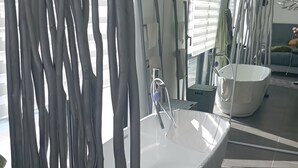 A modern bathroom with a freestanding bathtub, a shower area, and a large window with blinds. - Maison Contemporaine Avec Piscine, vue Dégagée (Draguignan)