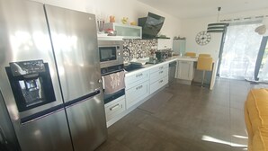 A modern kitchen with stainless steel appliances, a built-in oven, microwave, and a water dispenser. There is a patterned backsplash, a yellow chair, and a clock on the wall. - Maison Contemporaine Avec Piscine, vue Dégagée (Draguignan)
