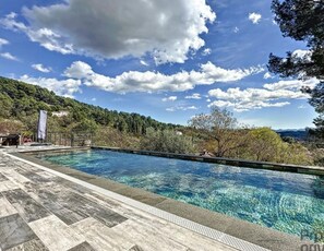 A swimming pool with clear water, surrounded by a wooden deck and a view of a forested hillside. - Maison Contemporaine Avec Piscine, vue Dégagée (Draguignan)