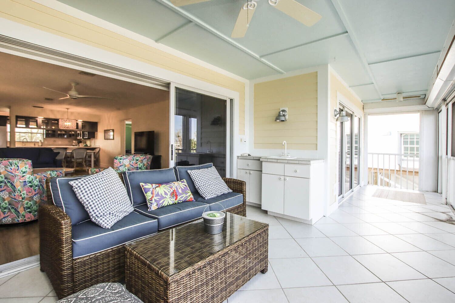 A spacious living area with a sofa, coffee table, and wicker furniture. A kitchen with white cabinets and a sink is visible in the background.