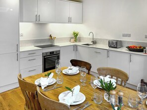 A modern kitchen with white cabinets, a built-in oven, and a dining area set for four with wooden chairs and a wooden table.