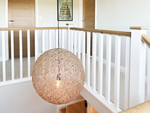 A staircase with a white railing, a woven pendant light, and a framed picture on the wall.