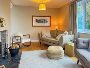 A cozy living room with a sofa, a chair, a fireplace, and a window with curtains.
