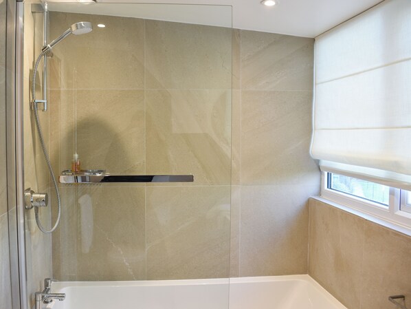 Un baño moderno con ducha, bañera y ventana con persianas.