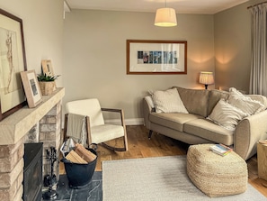 Una sala de estar con chimenea, un sofá, una silla, un tapete y una lámpara colgante.