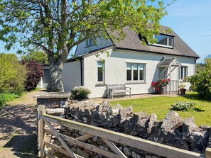 A white house with a stone wall, a bench, and a garden.