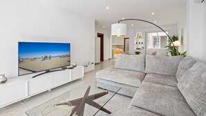 En moderne stue med et stort fladskærms-tv, en grå sofa og et hvidt tv-møbel.