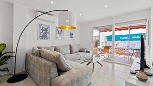 En moderne stue med en grå sofa, en gulvlampe og et sofabord i glas.
