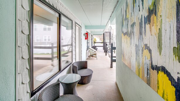 A corridor with wicker chairs and tables, a staircase, and a colorful mural on the wall. - Wildwood Condo: Community Pool, Walk to Beach! (Wildwood)