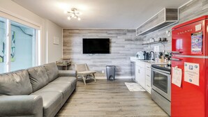 A modern kitchen with a red refrigerator, a flat-screen TV mounted on the wall, and a grey leather sofa in the living area. - Wildwood Condo: Community Pool, Walk to Beach! (Wildwood)