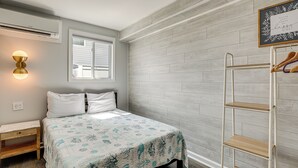 A bedroom with a bed, bedside table, wall-mounted shelf, and a window with blinds. - Wildwood Condo: Community Pool, Walk to Beach! (Wildwood)