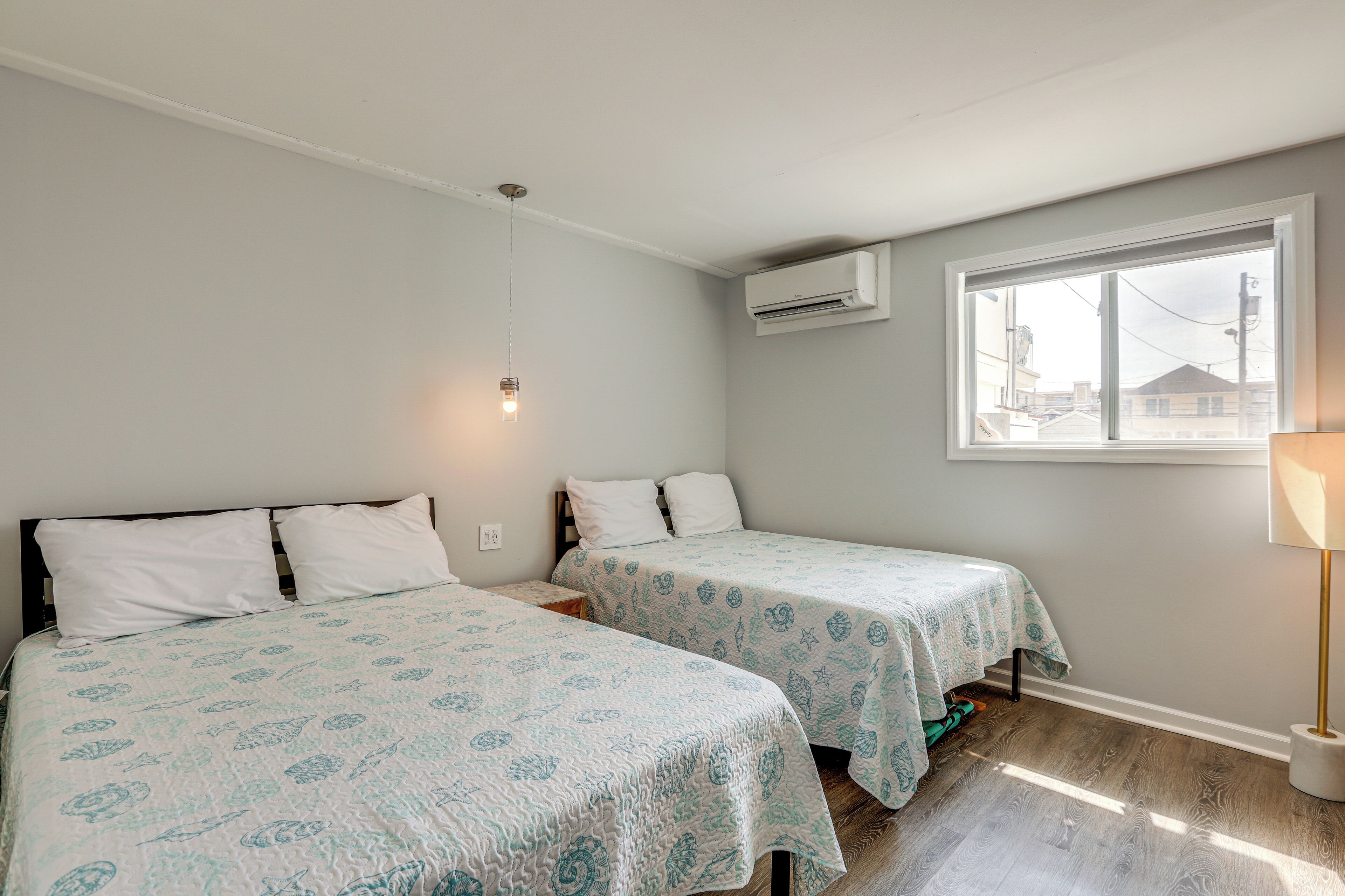 A bedroom with two beds, a window, an air conditioner, and a lamp.