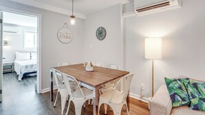 A dining area with a wooden table and white chairs, a wall clock, and a hanging sign. - Wildwood Condo: Community Pool, Walk to Beach! (Wildwood)