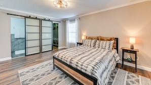 Une chambre à coucher comprenant un lit, une table de chevet, une lampe, un placard avec porte coulissante et un tapis à motifs.