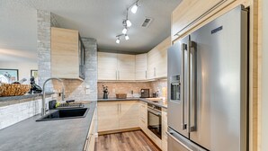Une cuisine moderne dotée d’un réfrigérateur en acier inoxydable, de meubles en bois, d’un four encastré et d’un mur décoratif en pierre.