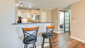 Une cuisine moderne avec un coin bar, deux tabourets et un lave-linge en arrière-plan.