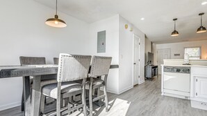 Ein Essbereich mit Holztisch und -stühlen, eine Küche mit weißen Geräten und Pendelleuchten.