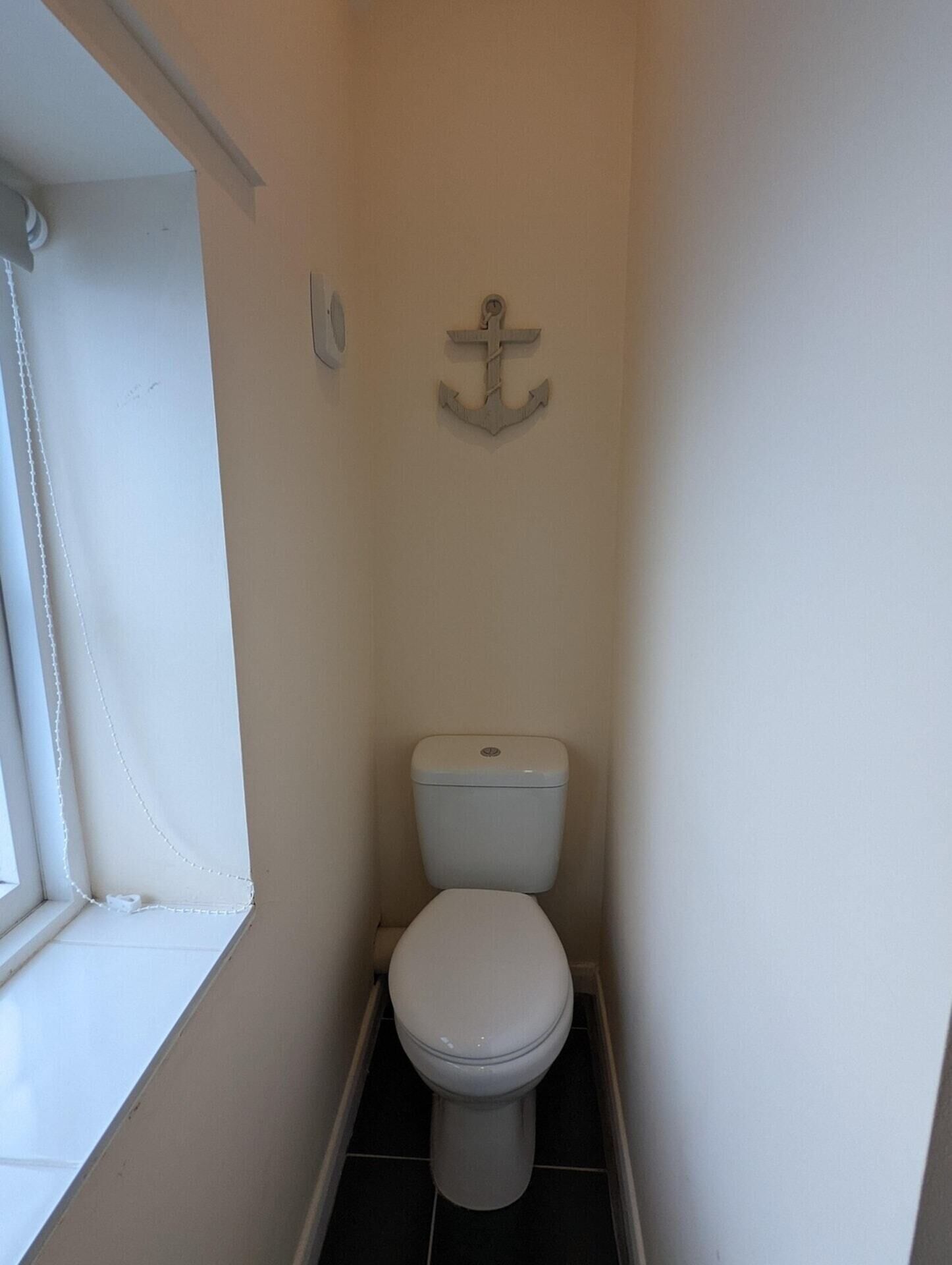 A small, narrow bathroom with a toilet, a window, and an anchor decoration on the wall.