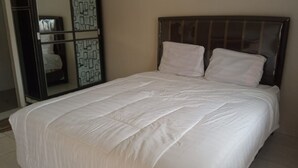 Una cama bien tendida con sábanas blancas en una habitación con piso de baldosas y un cabecero oscuro.