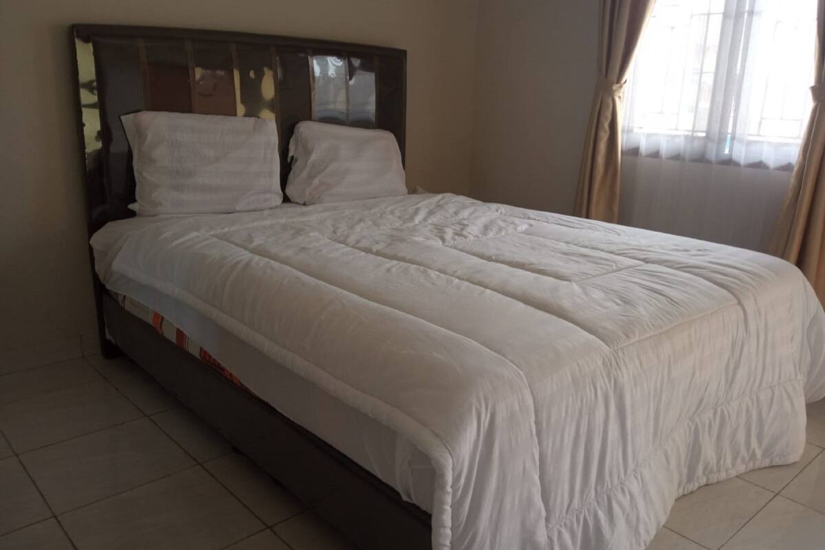 A bed with a wooden headboard, white bedding, and a window with curtains.