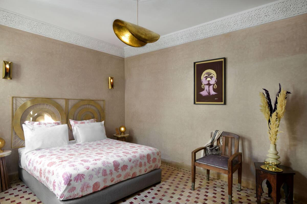 A hotel room with a large bed, a chair, a small table, and a decorative vase.
