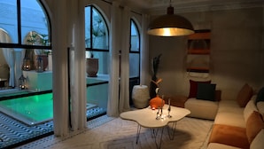 A modern living room with a white sofa, a white coffee table, and a large window with a view of a swimming pool. - Riad Palau Marrakech (Marrakech)
