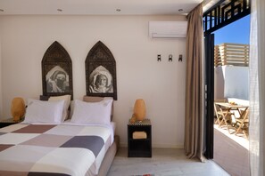 A bedroom with a large bed, two wall-mounted decorative items, a small table with chairs, and a balcony with a wooden railing. - Riad Palau Marrakech (Marrakech)