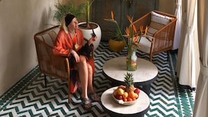 A room with a patterned floor, a wicker chair, a round table with a fruit bowl, and a potted plant. - Riad Palau Marrakech (Marrakech)