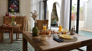 A dining table with breakfast items, a vase, and a view of an outdoor pool area. - Riad Palau Marrakech (Marrakech)
