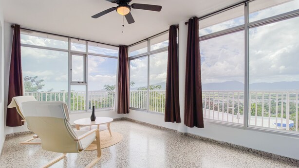 A spacious room with large windows, a ceiling fan, a round table, and a chair.