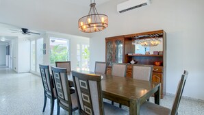 A spacious dining area with a wooden table and chairs, a chandelier, and a wooden cabinet with glass doors.