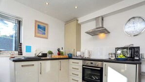A modern kitchen with white cabinets, a black countertop, a stainless steel oven, and a wall-mounted clock.